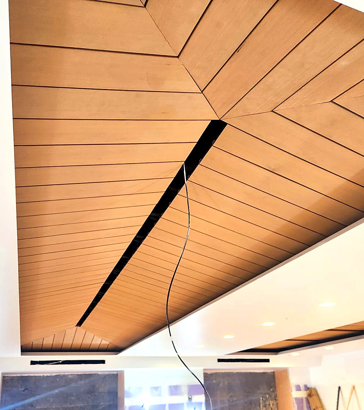 Chevron-pattern wood plank ceiling with recessed linear lighting reveal