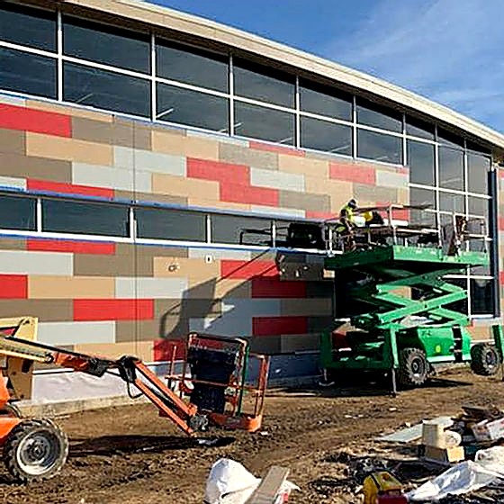 Crew installing multi-tone panel facade on a new commercial building from lifts