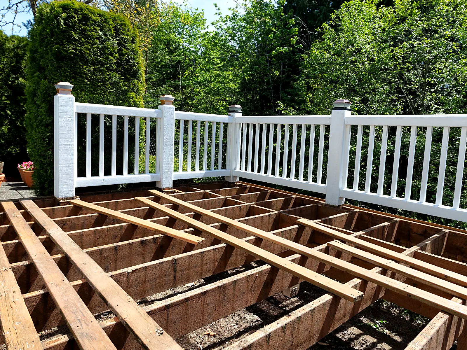 Deck restoration with boards removed exposing framing beneath a white railing