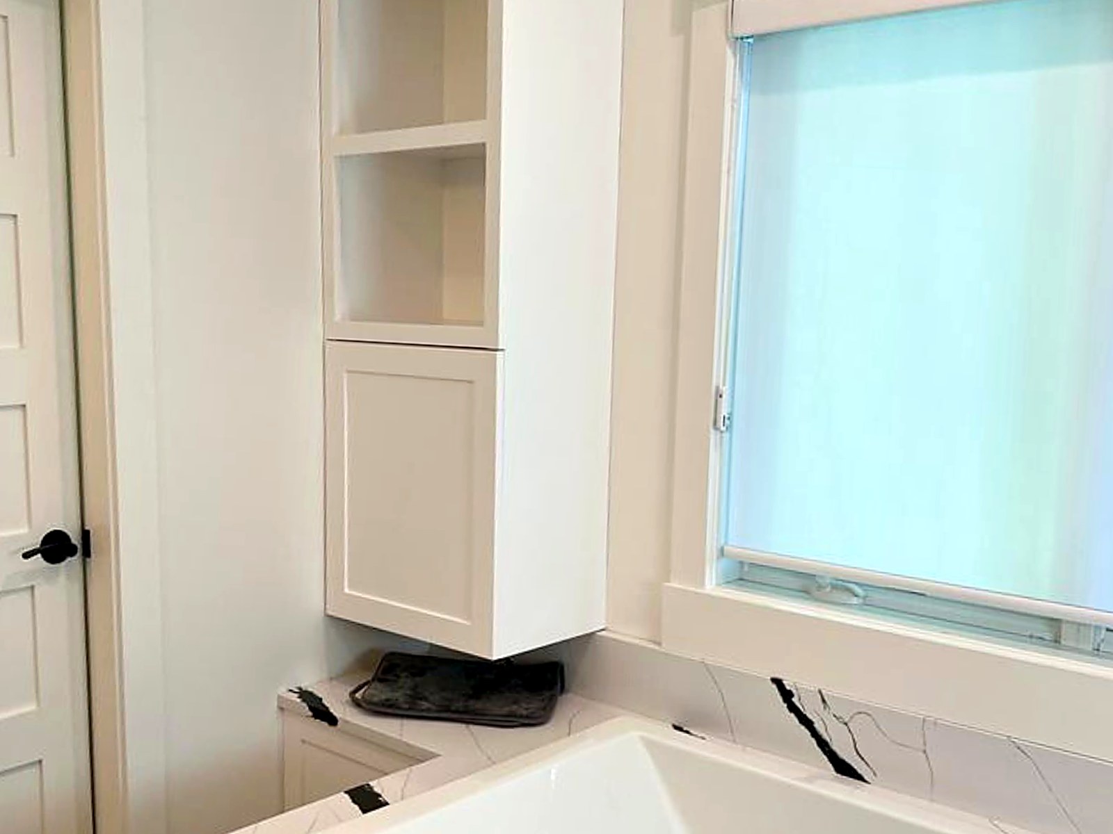Custom bathroom linen tower with open shelving above a quartz tub deck