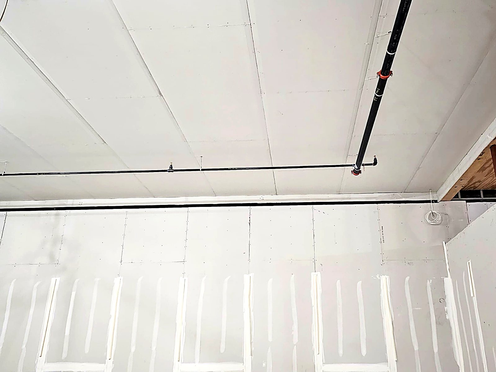 High drywall wall and ceiling with taped joints below sprinkler piping