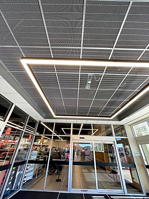 Open metal mesh ceiling with linear LED perimeter lighting at a retail entrance