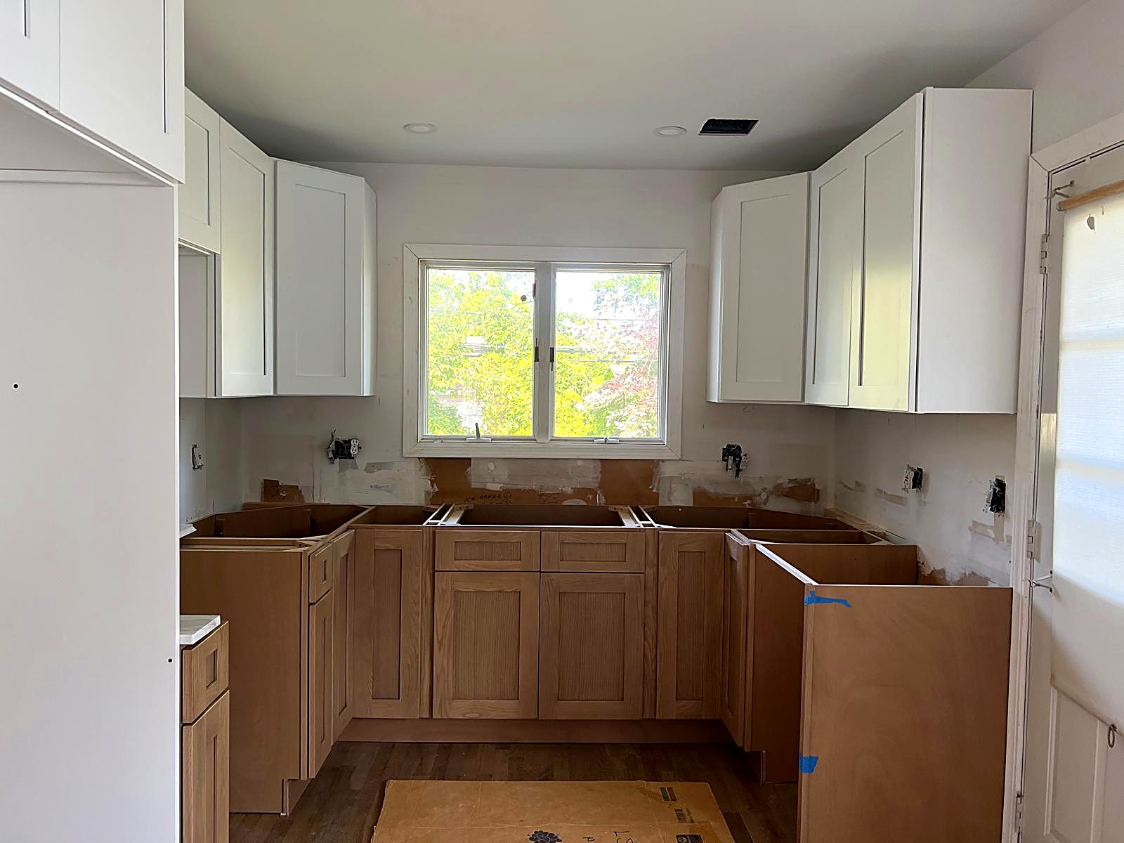 Kitchen millwork installation with white upper cabinetry and oak base cabinets set to layout