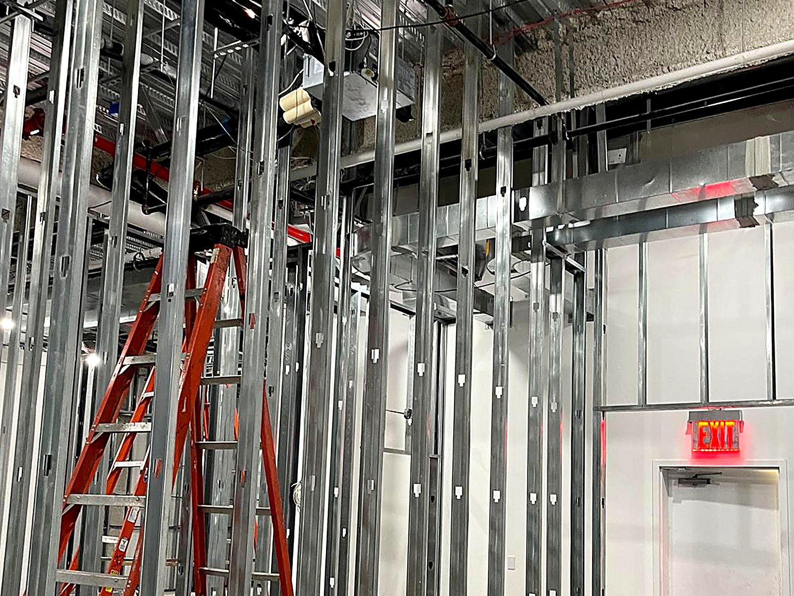 Metal stud corridor framing beside a finished exit door and overhead mechanicals