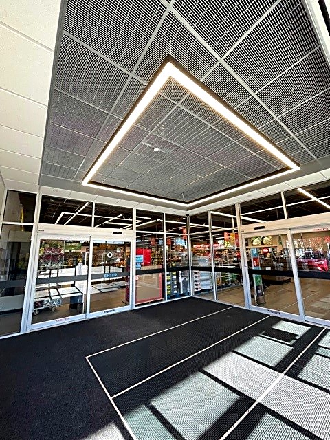 Metal grille ceiling and floating illuminated light frame in a commercial vestibule