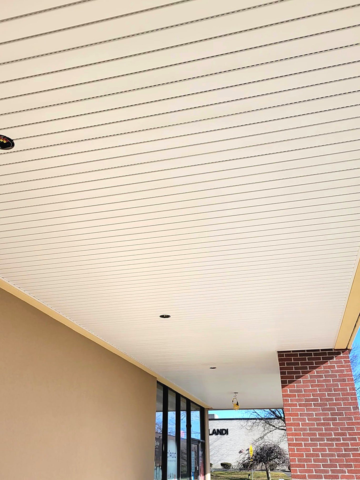 Linear metal plank soffit ceiling with integrated vents at a retail entrance canopy