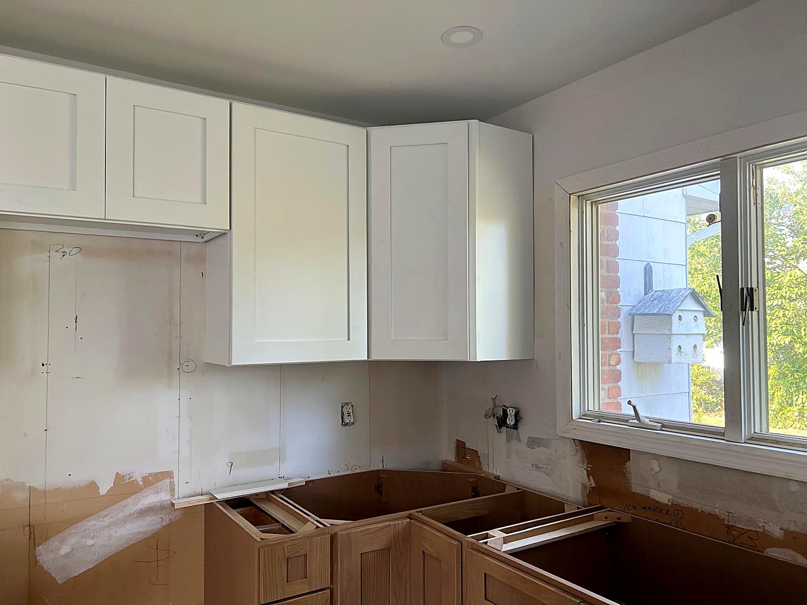 Shaker wall cabinets installed plumb at a corner return beside a window casing