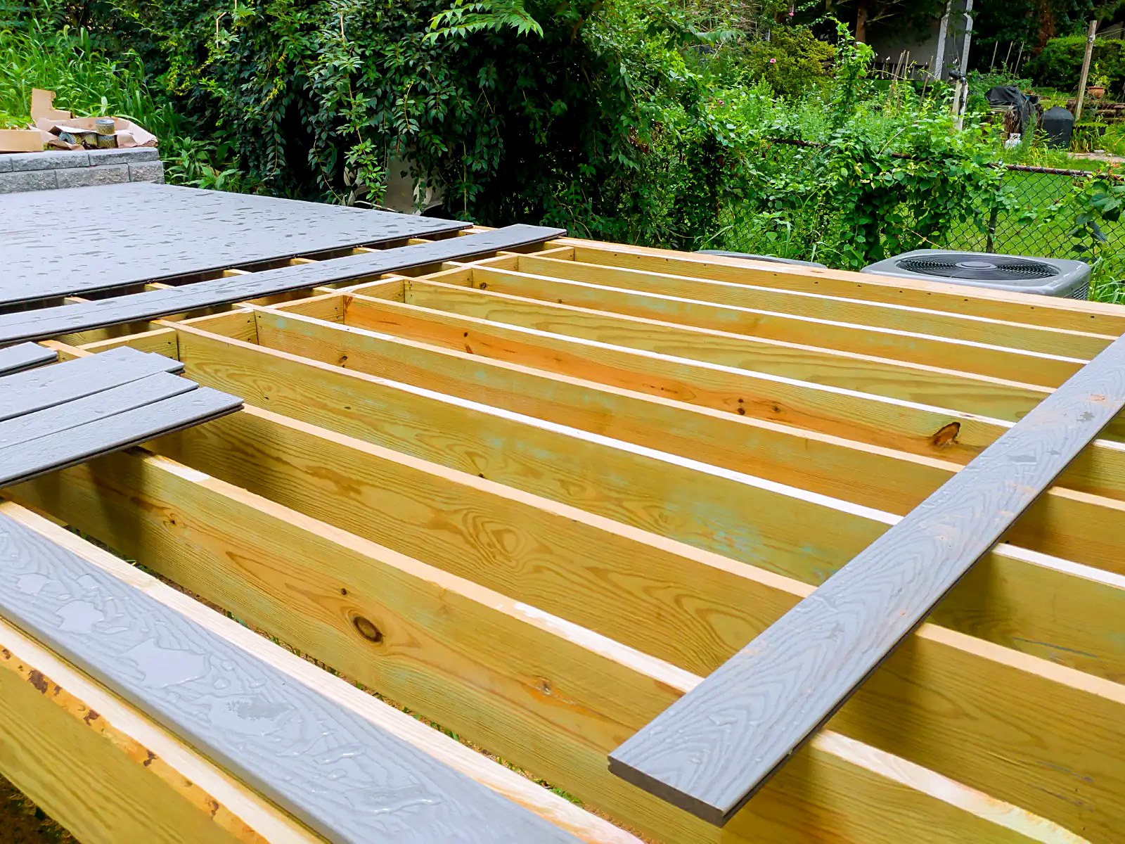 Gray composite deck boards being laid over new pressure-treated framing