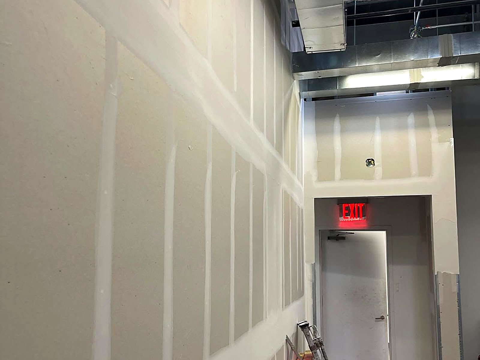 Tall drywall corridor walls taped and finished beside an exit door