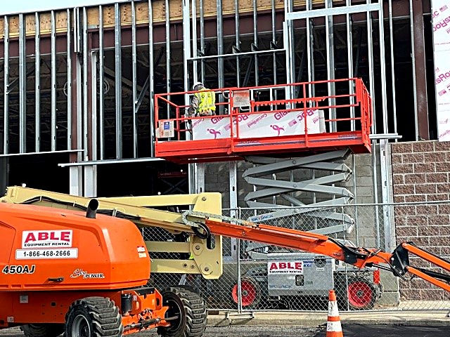 Crew working from a scissor lift on exterior sheathing and framing of a retail building shell