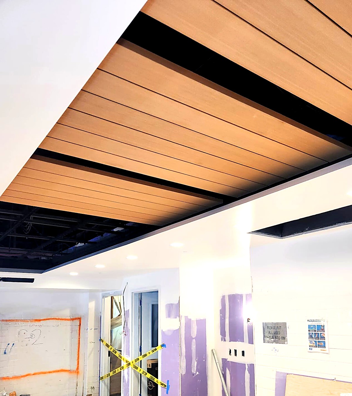 Wood plank ceiling panel with black reveals set into a finished gypsum ceiling