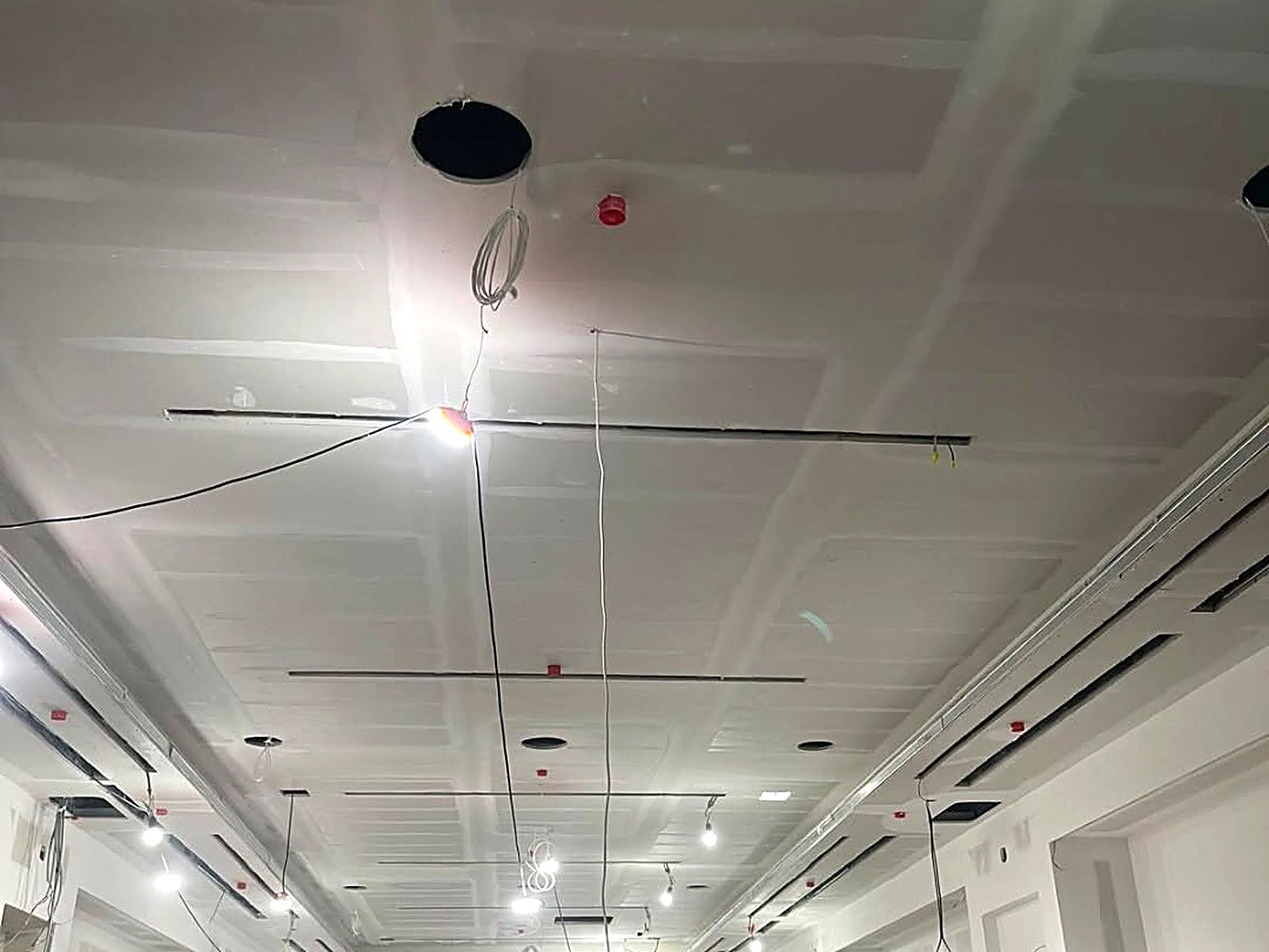 Long commercial corridor with finished drywall ceiling and light rough-in