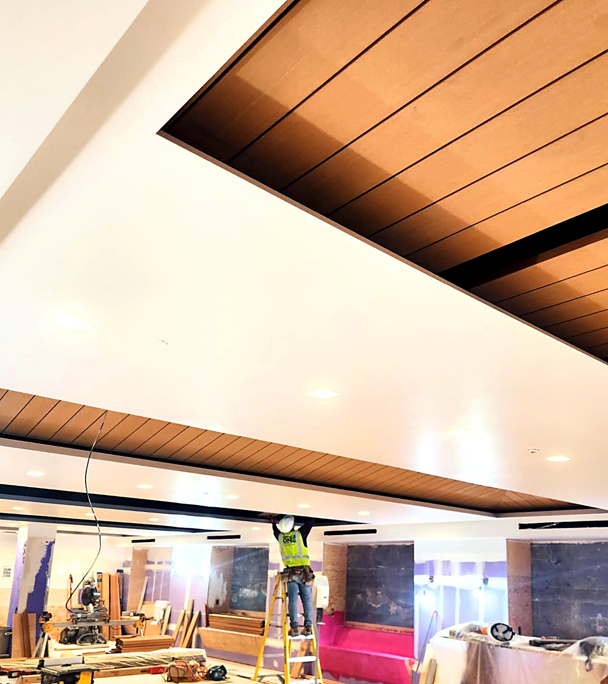 Wood plank ceiling feature and gypsum bulkhead being installed by a carpenter